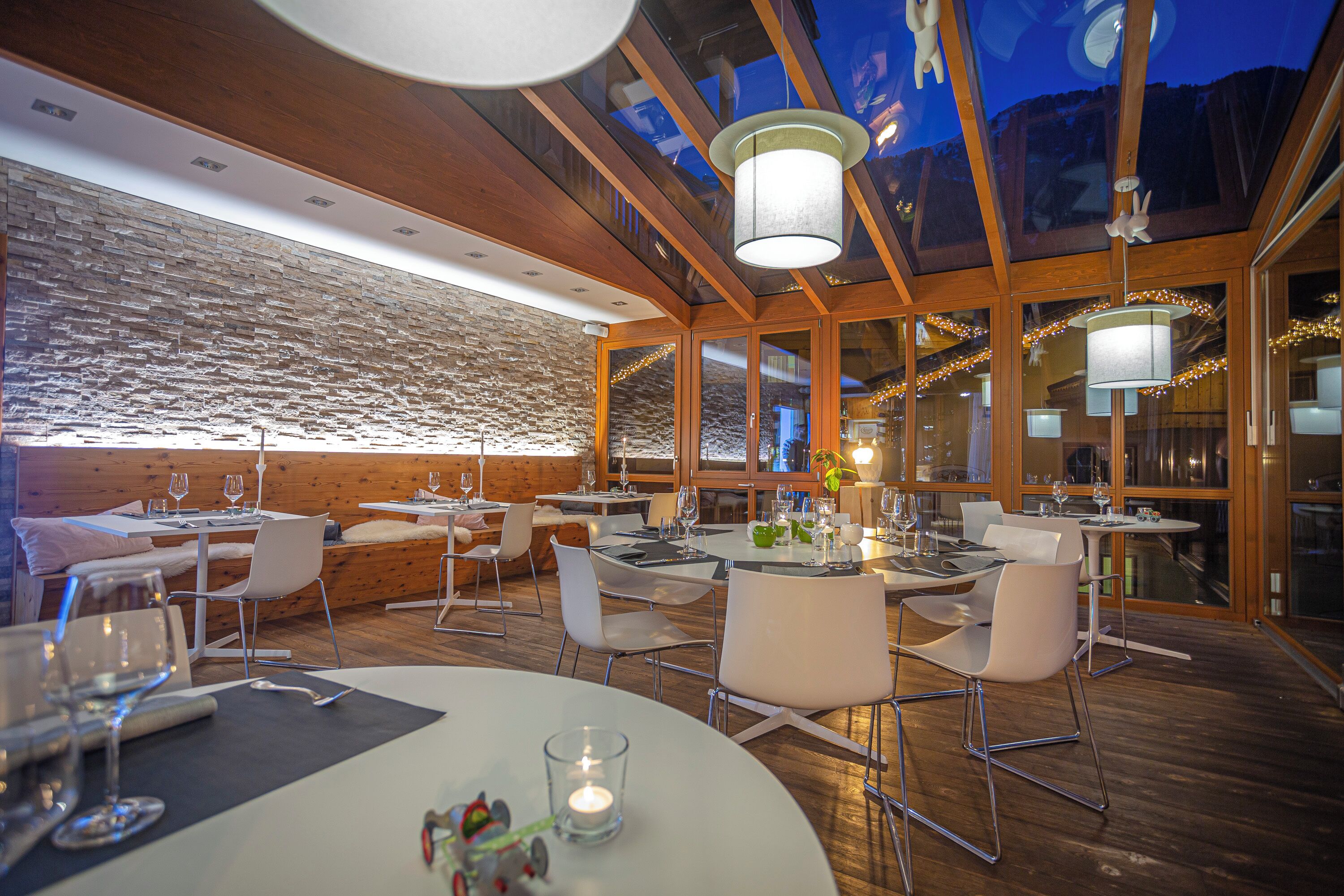 A restaurant with wooden interiors, glass walls, and multiple dining tables with chairs.