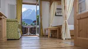 Una habitación con piso de madera, una mesa de comedor con sillas, un banco, un radiador y vistas a montañas a través de un amplio ventanal.