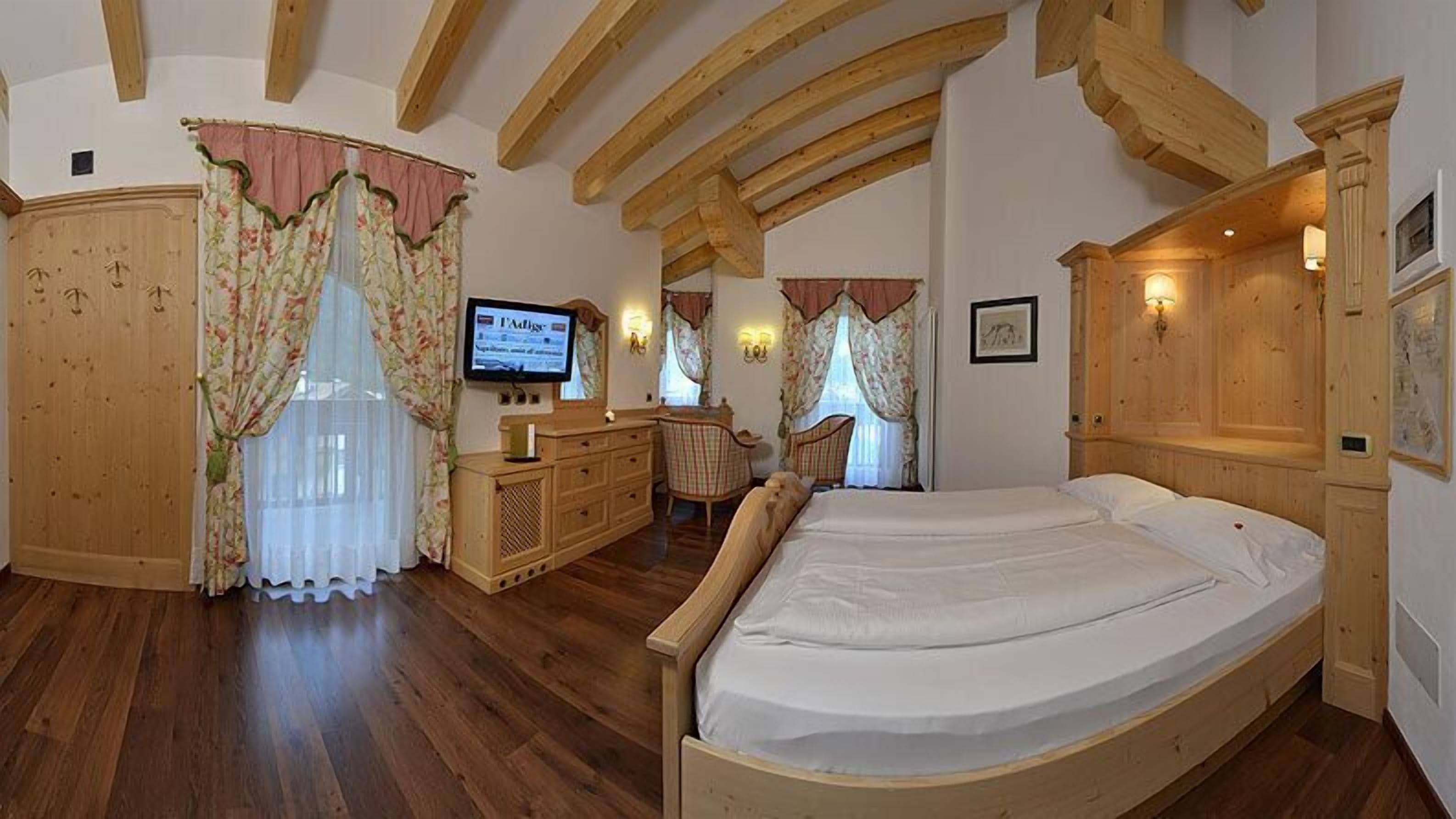 Un dormitorio con vigas de madera, una cama, un aparador, un televisor y un escritorio con una silla.
