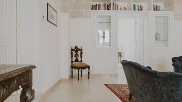 Une pièce avec une table en bois, un fauteuil à l’assise rembourrée de couleur sombre, un tapis à motifs et une bibliothèque remplie de livres.