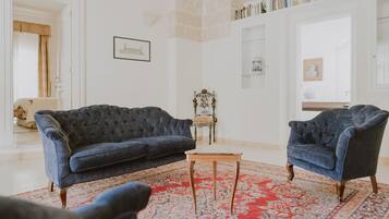 A living room with a dark blue sofa, a matching armchair, and a wooden coffee table. A red and blue patterned rug covers the floor.
