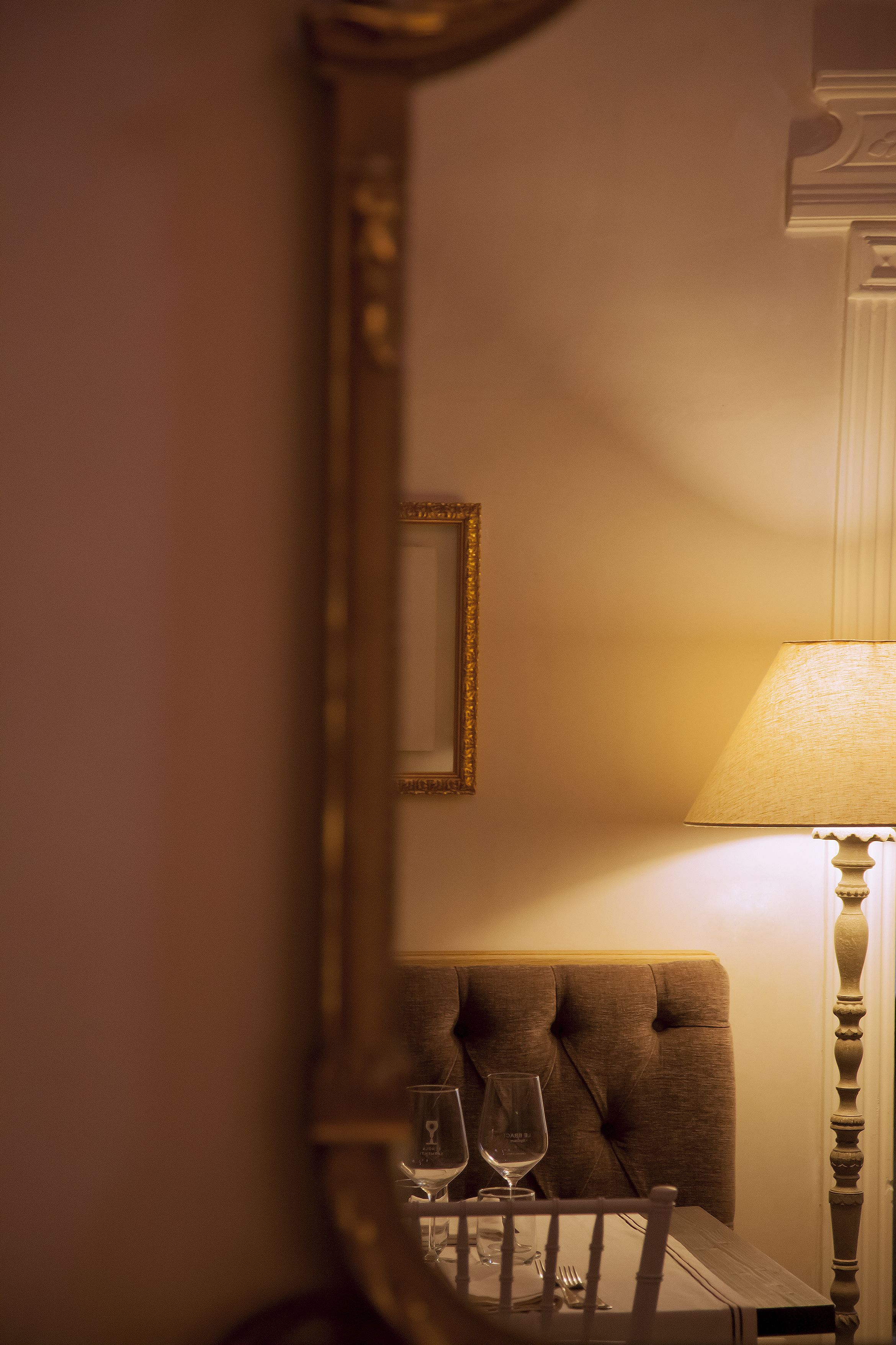 A dining table with two wine glasses and a fork, set against a wall with a mirror and a lamp.