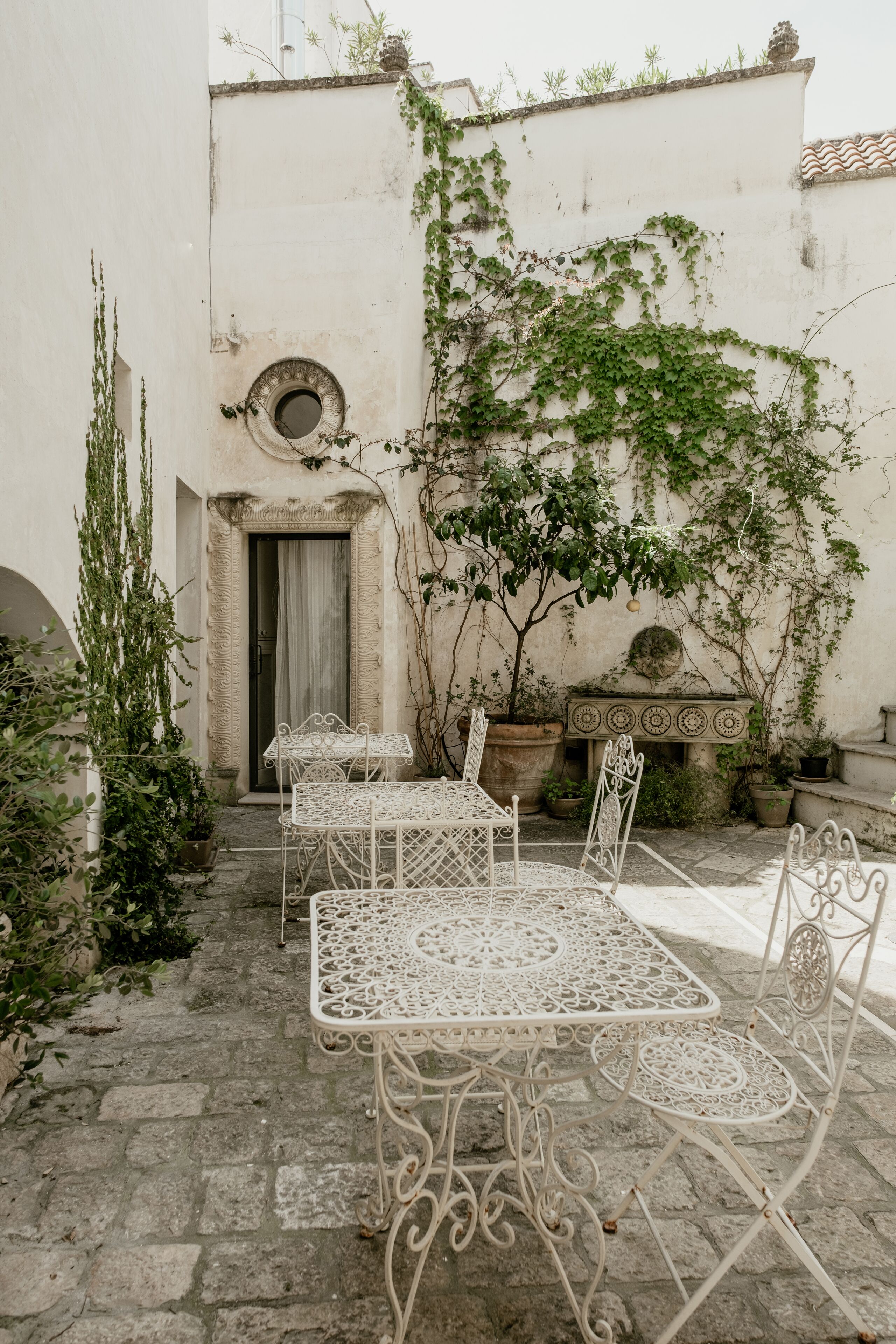 A courtyard with a white metal table and chairs, a potted plant, and a stone bench.