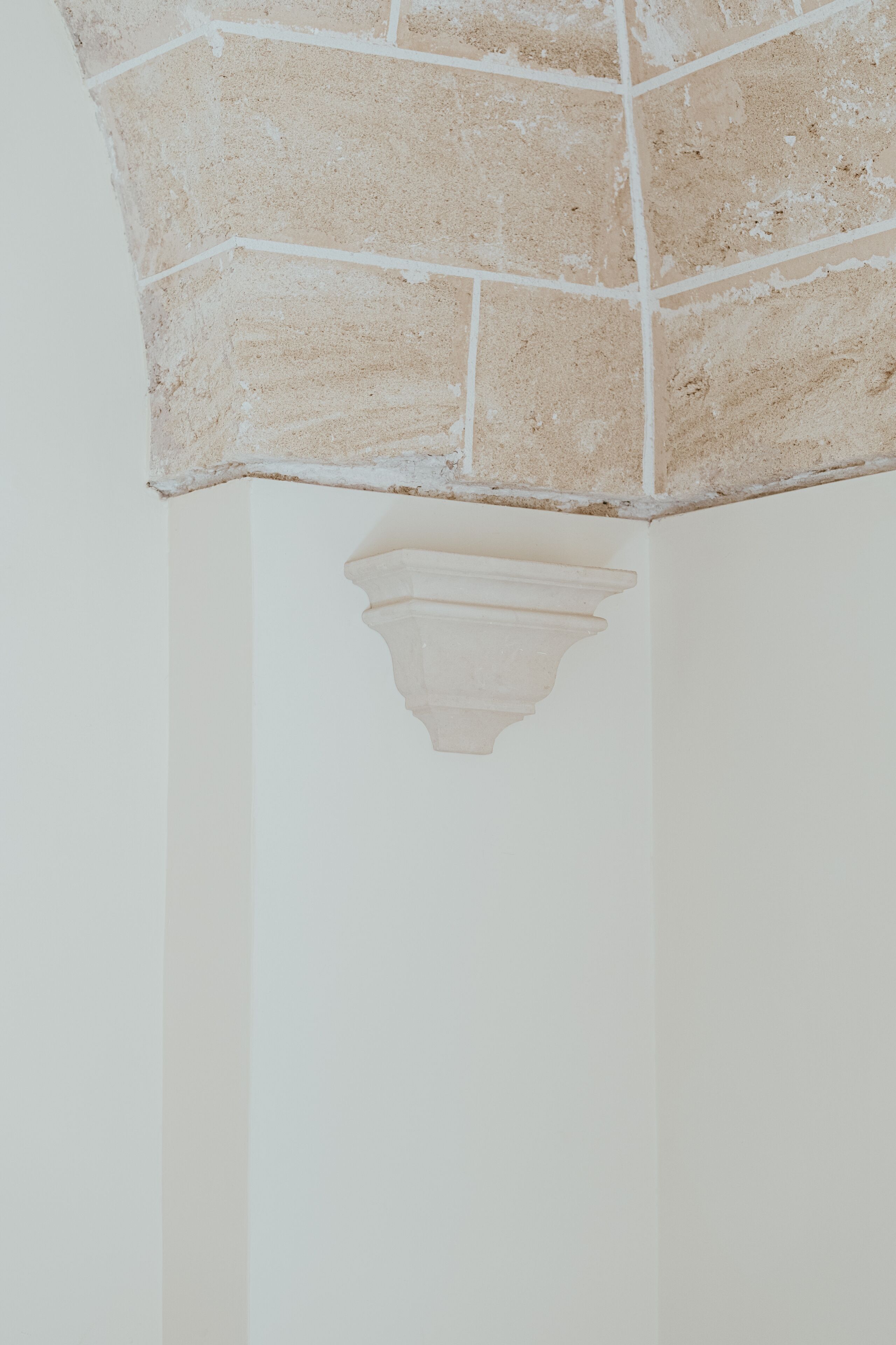 A corner of a room with a white wall and a section of exposed brickwork.