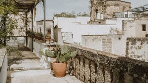 A rooftop terrace with a pergola, potted plants, and a view of historic buildings. - Relais Il Mignano (Nardò)