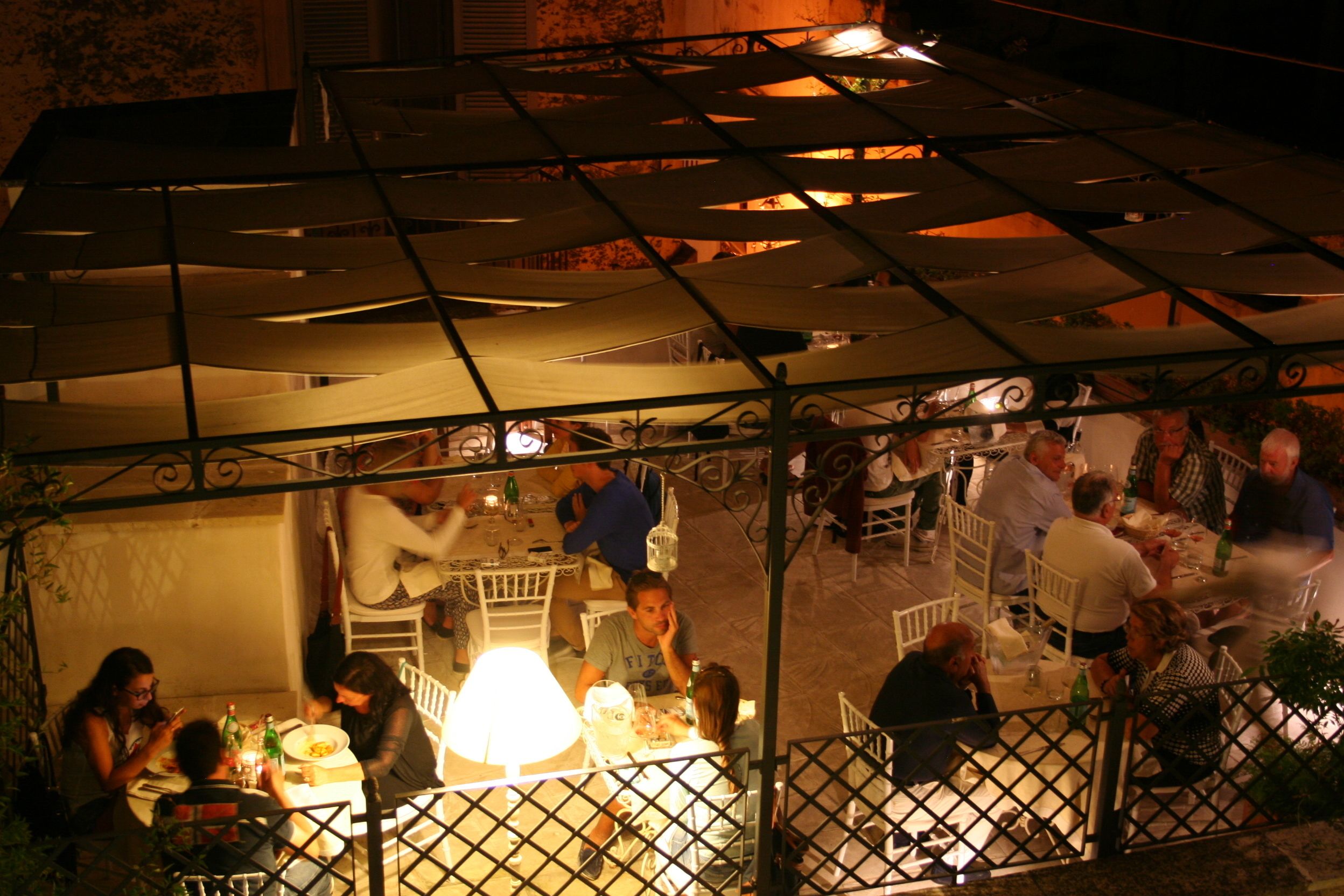 An outdoor dining area with tables and chairs, a metal roof structure, and a decorative fence.