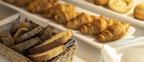 A buffet with various baked goods including bread, croissants, and pastries.
