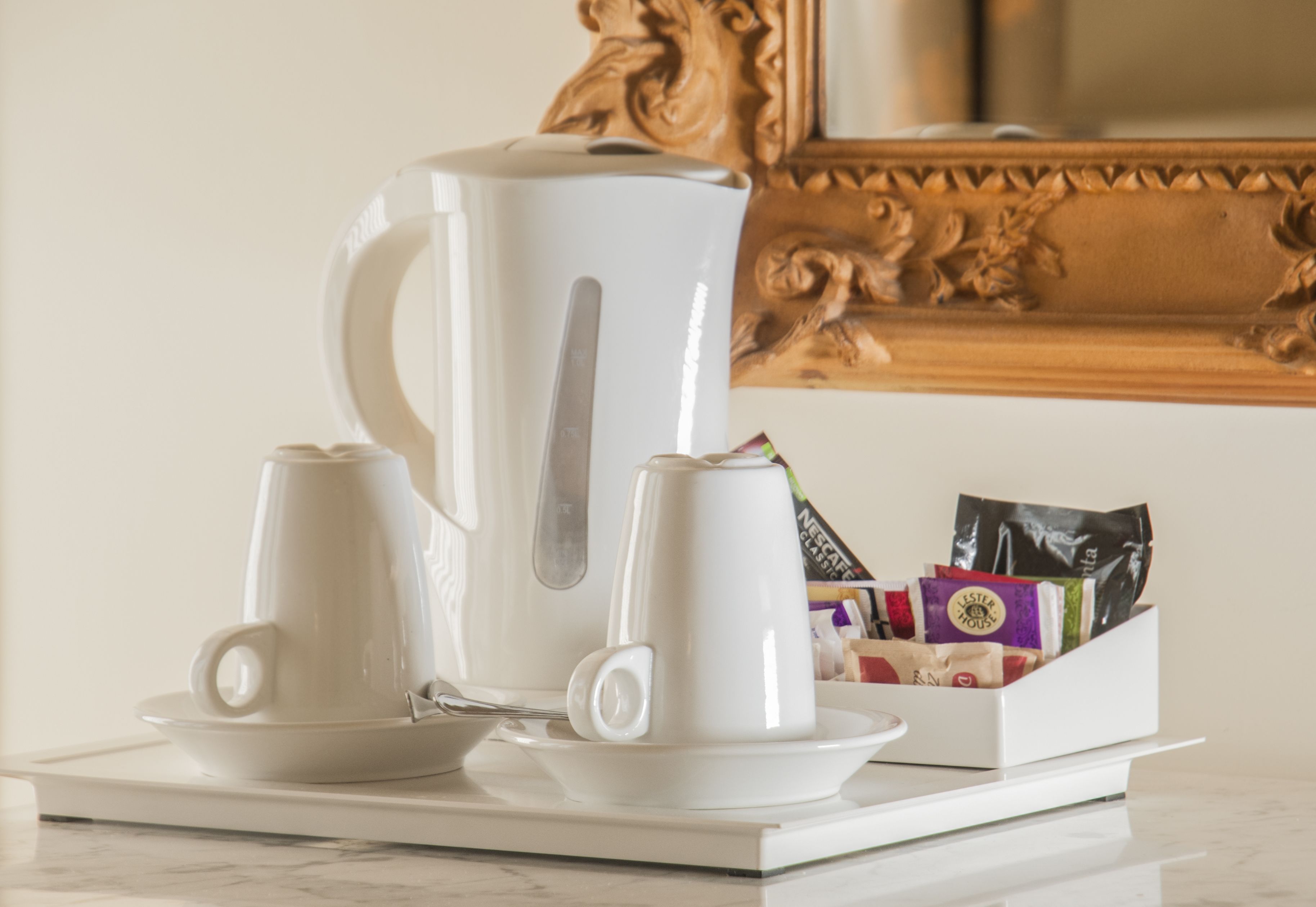 A coffee station with two white cups, a white coffee pot, and a box of coffee packets.