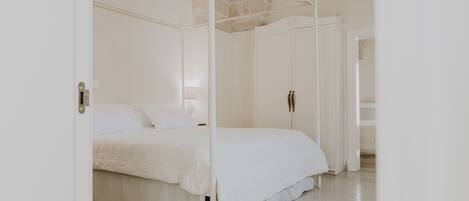 Un dormitorio con cama con dosel, alfombra roja estampada y paredes blancas.