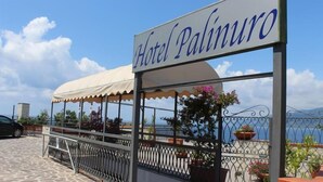 A hotel sign reading "Hotel Palinuo" with a covered outdoor seating area and potted plants. - Hotel Palinuro (Centola)