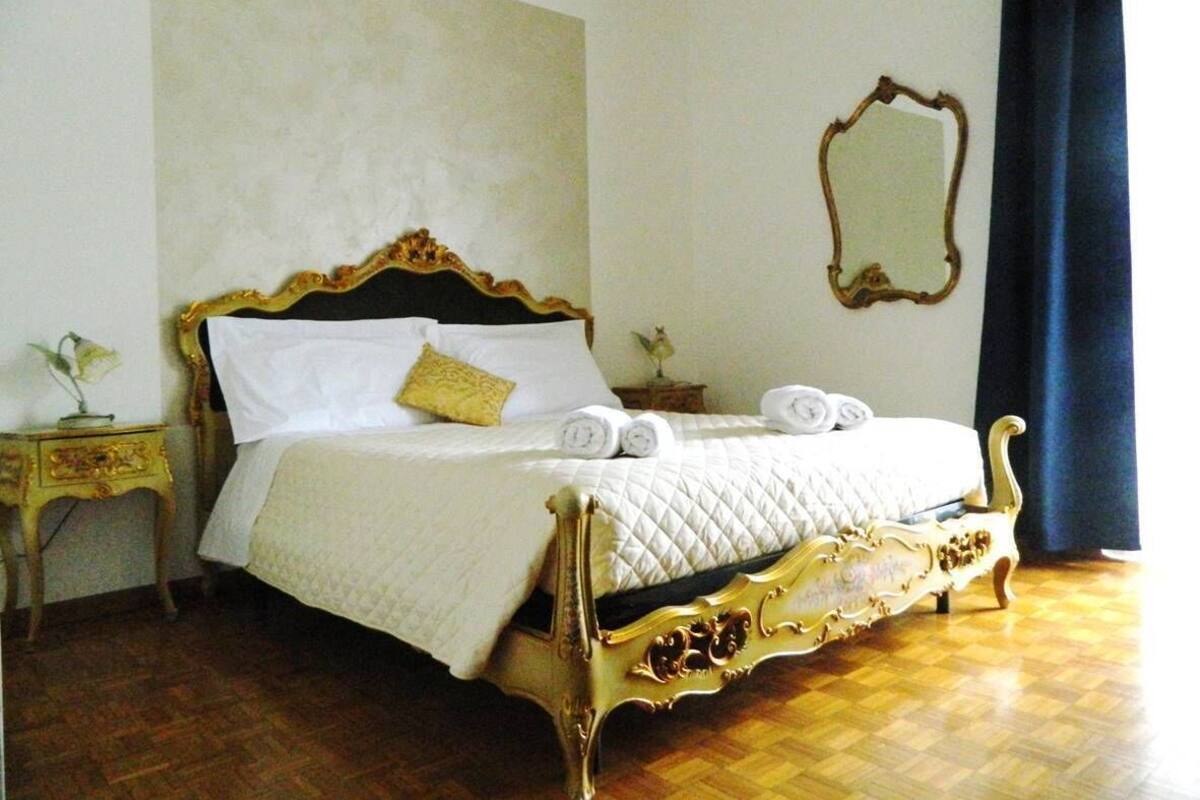 Una cama con detalles dorados ornamentales, un edredón blanco y dos almohadas.