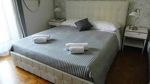 A neatly made bed with two towels, a bedside table with a lamp, and patterned wallpaper. - B&B Tosca (Verona)