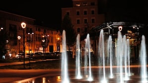 A nighttime fountain with multiple water jets in a public square, surrounded by buildings with illuminated windows. - B&B Tosca (Verona)