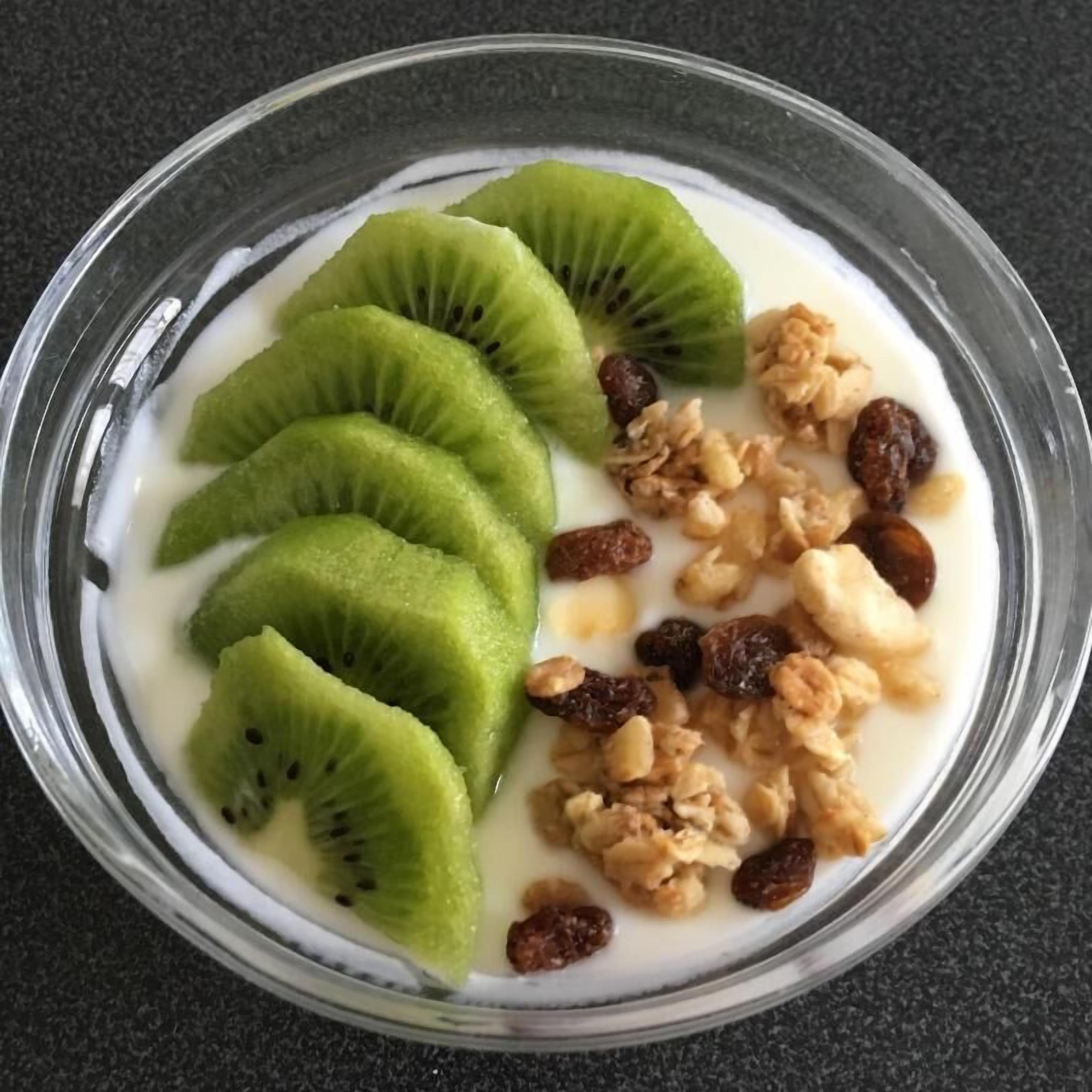 A bowl of yogurt with kiwi slices, raisins, and walnuts.