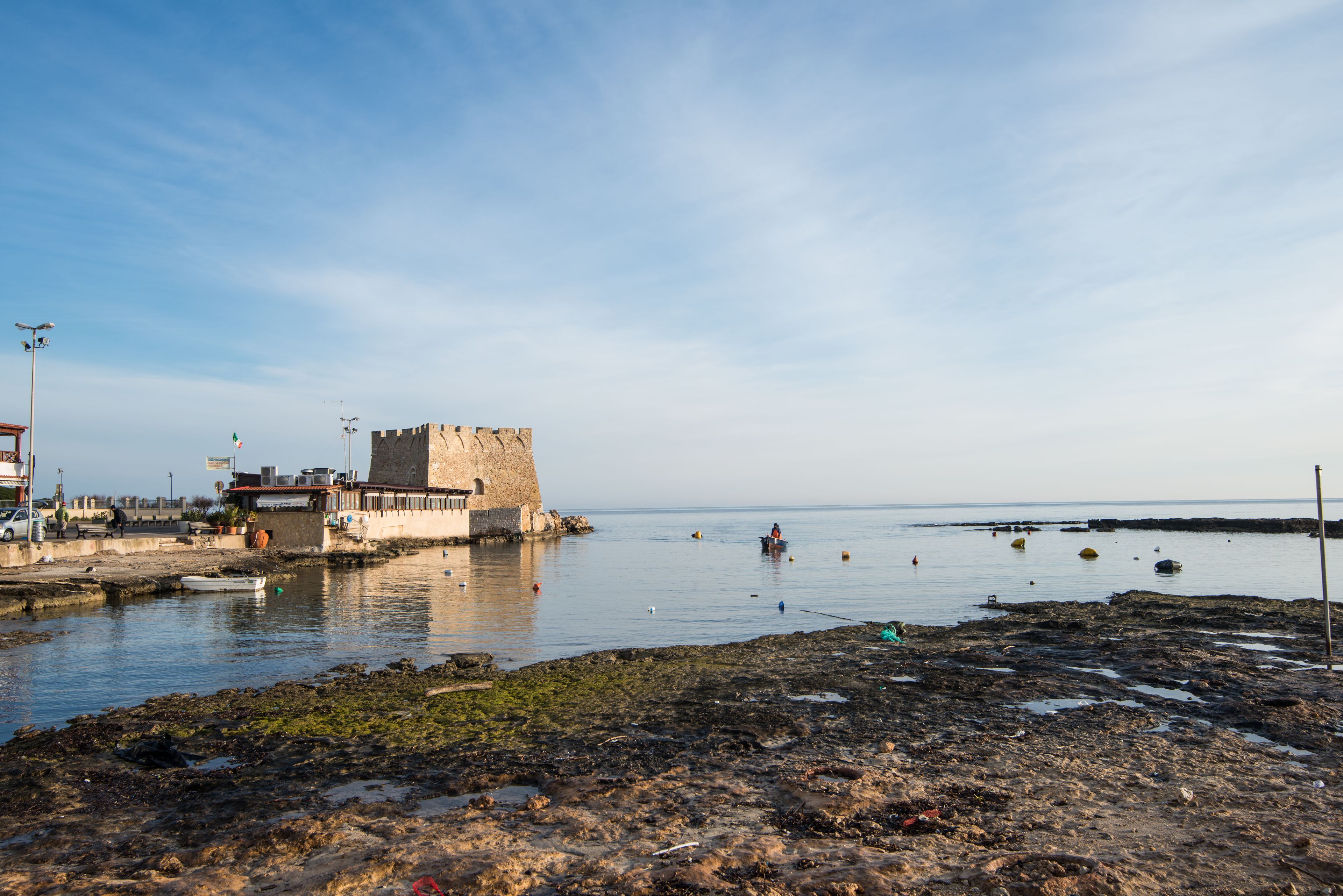Una zona costera con un edificio histórico de piedra, un litoral rocoso y aguas tranquilas.