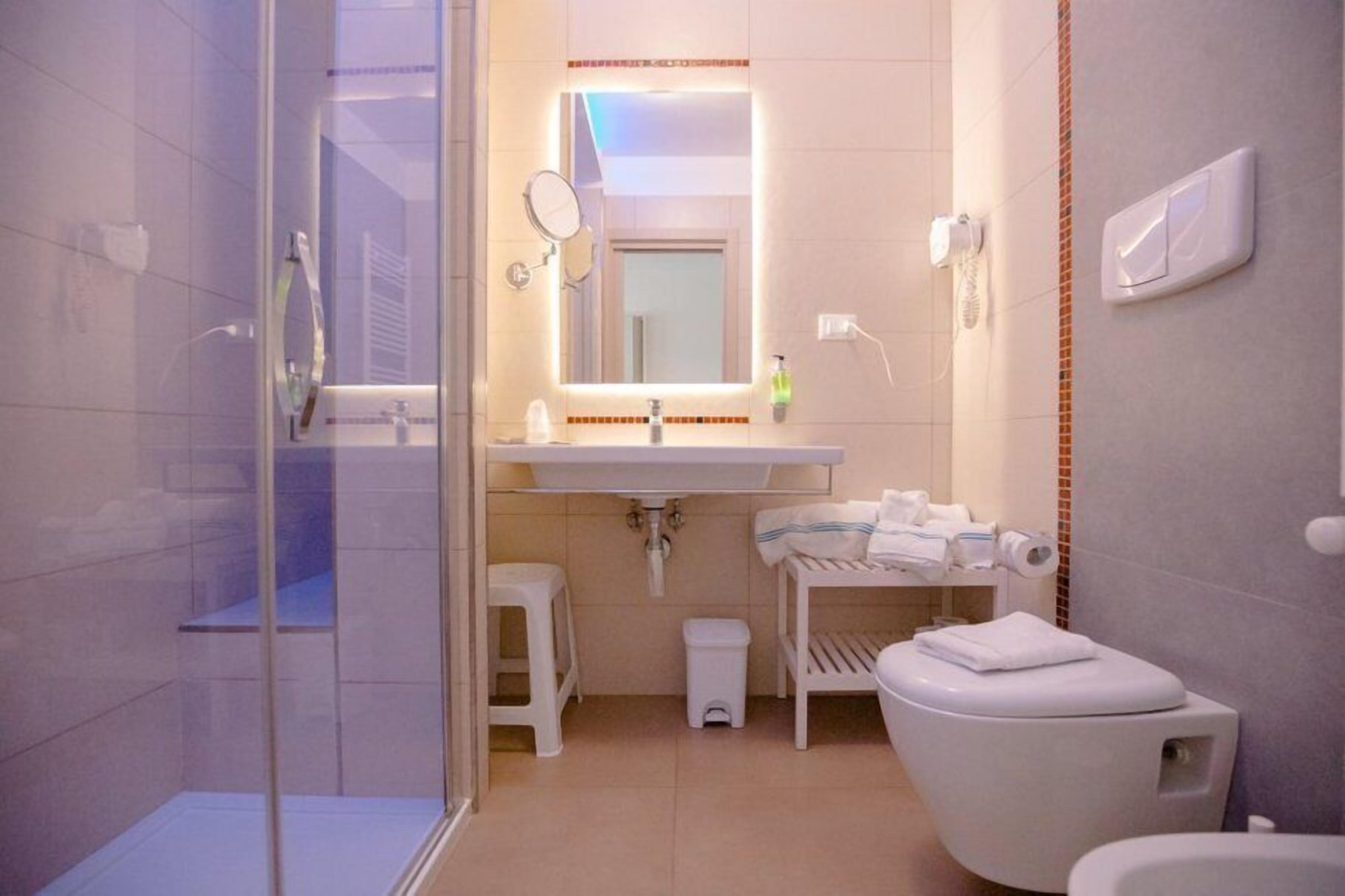 Ein modernes Badezimmer mit Duschkabine aus Glas, einem weißen Waschbecken mit Spiegel und einer Toilette.