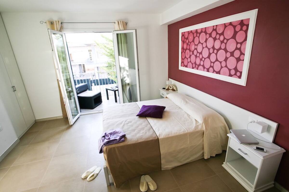 A bedroom with a bed, a nightstand, a laptop, and slippers on the floor.