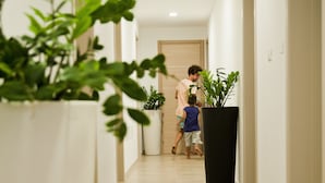 A hallway with a potted plant on the left, a man and a child walking towards a door, and a large black planter on the right. - CiCò Hotel (Carovigno)