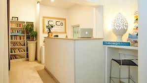 A reception area with a desk, a laptop, a framed sign, a bookshelf, and a potted plant. - CiCò Hotel (Carovigno)