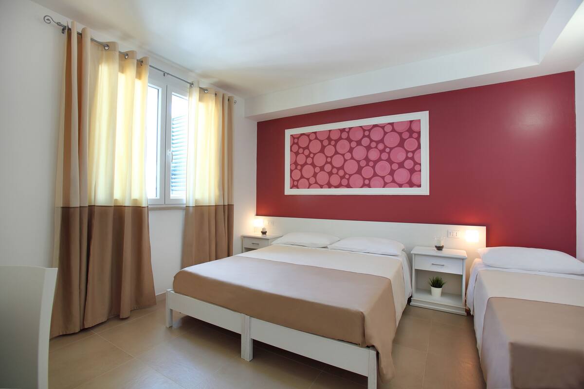 A hotel room with a large bed, two bedside tables, a nightstand, and a window with curtains.