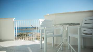 Un balcón con sillas y una mesa blancos, con vista a una playa y al océano.