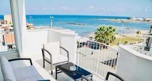 Ein Balkon mit Blick auf das Meer, weiße Möbel und ein kleiner Tisch.
