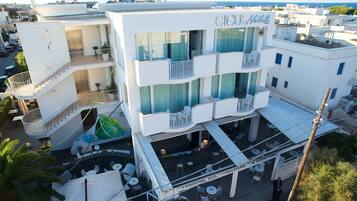 Un hotel de varios pisos con balcones, mobiliario exterior y una zona de piscina visible.