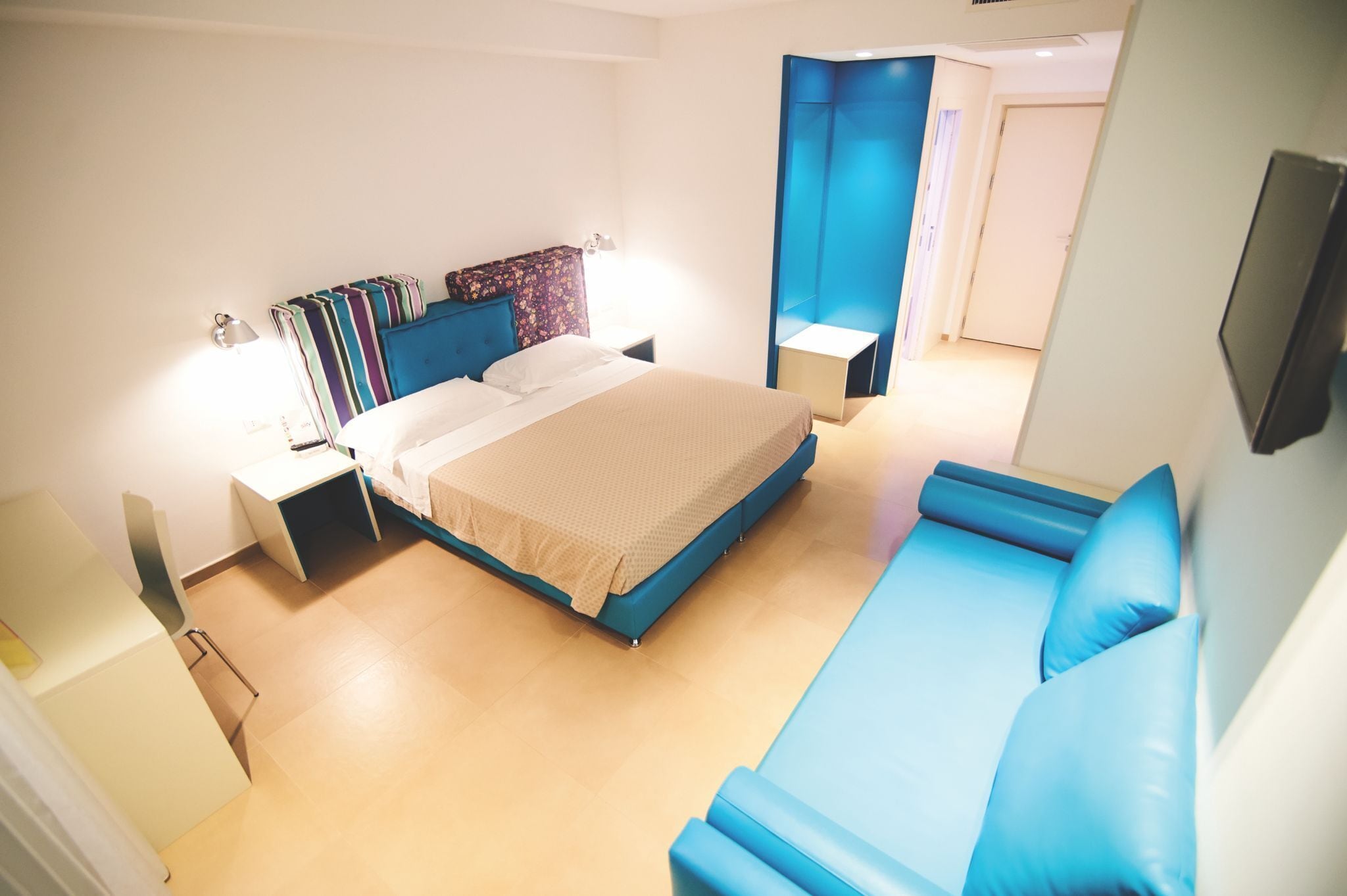 Une chambre d’hôtel moderne avec un lit, un canapé bleu, une table de chevet et un bureau.