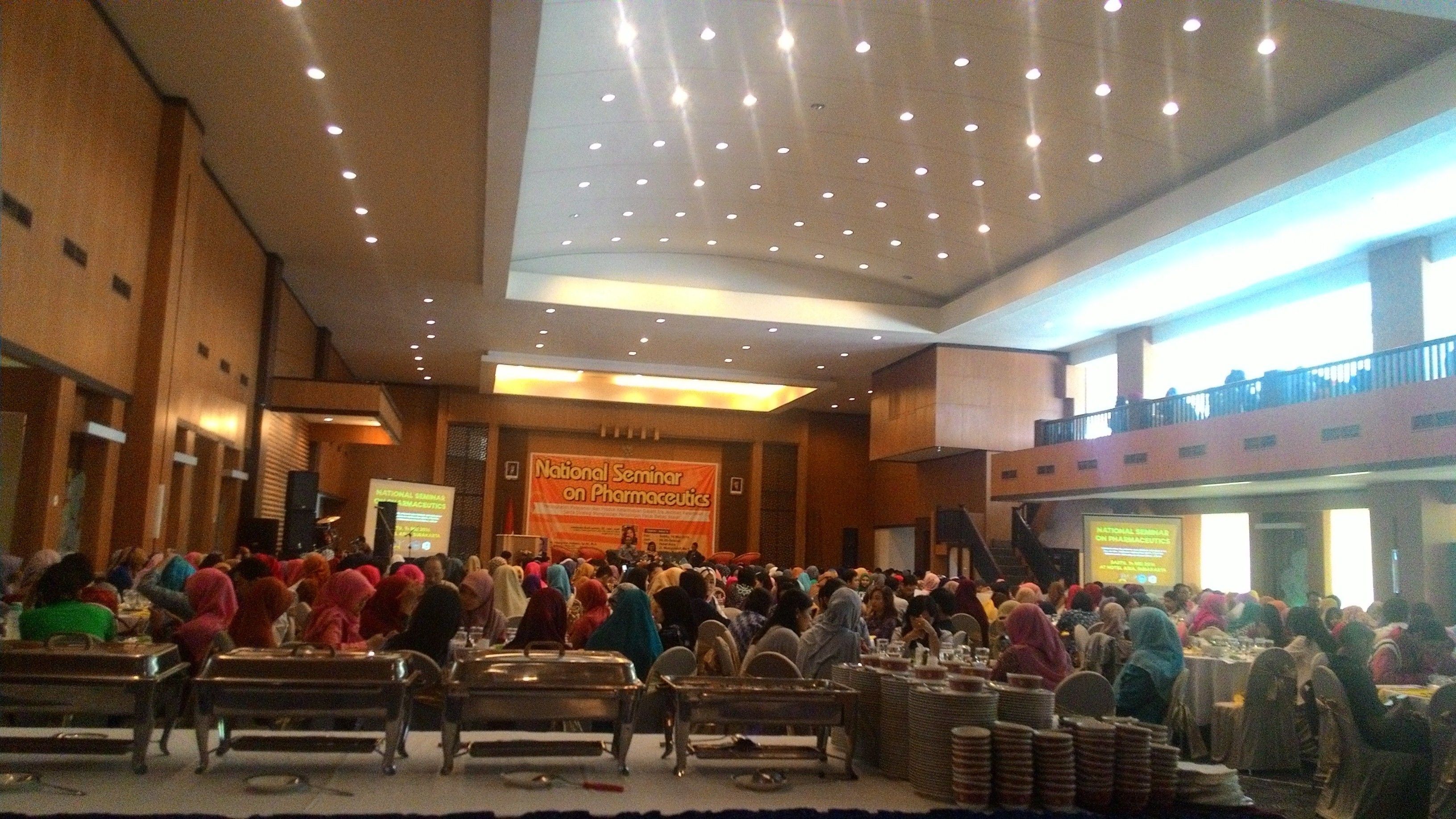 A large indoor gathering space with tiered seating and a stage for presentations.