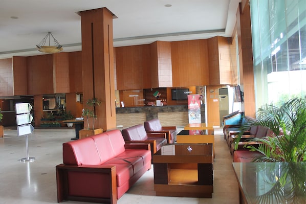 A hotel lobby with red leather sofas, wooden reception desk, and a large window offering a view of the outdoors. - Hotel Asia (Surakarta)