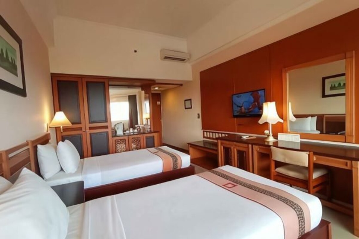 Ein Hotelzimmer mit zwei Betten, einem Schreibtisch, einem Stuhl, einem Spiegel und einem Fernseher.