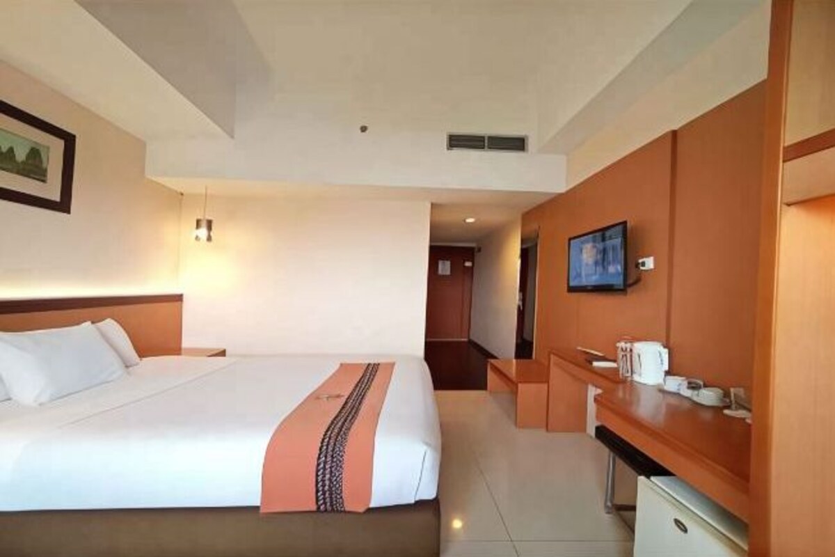 Ein Hotelzimmer mit einem großen Bett, einem Schreibtisch, einem Fernseher und einer Küchenzeile.