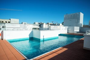 Ein Pool auf dem Dach mit klarem, blauem Wasser, umgeben von weißen Wänden und einer gefliesten Terrasse.