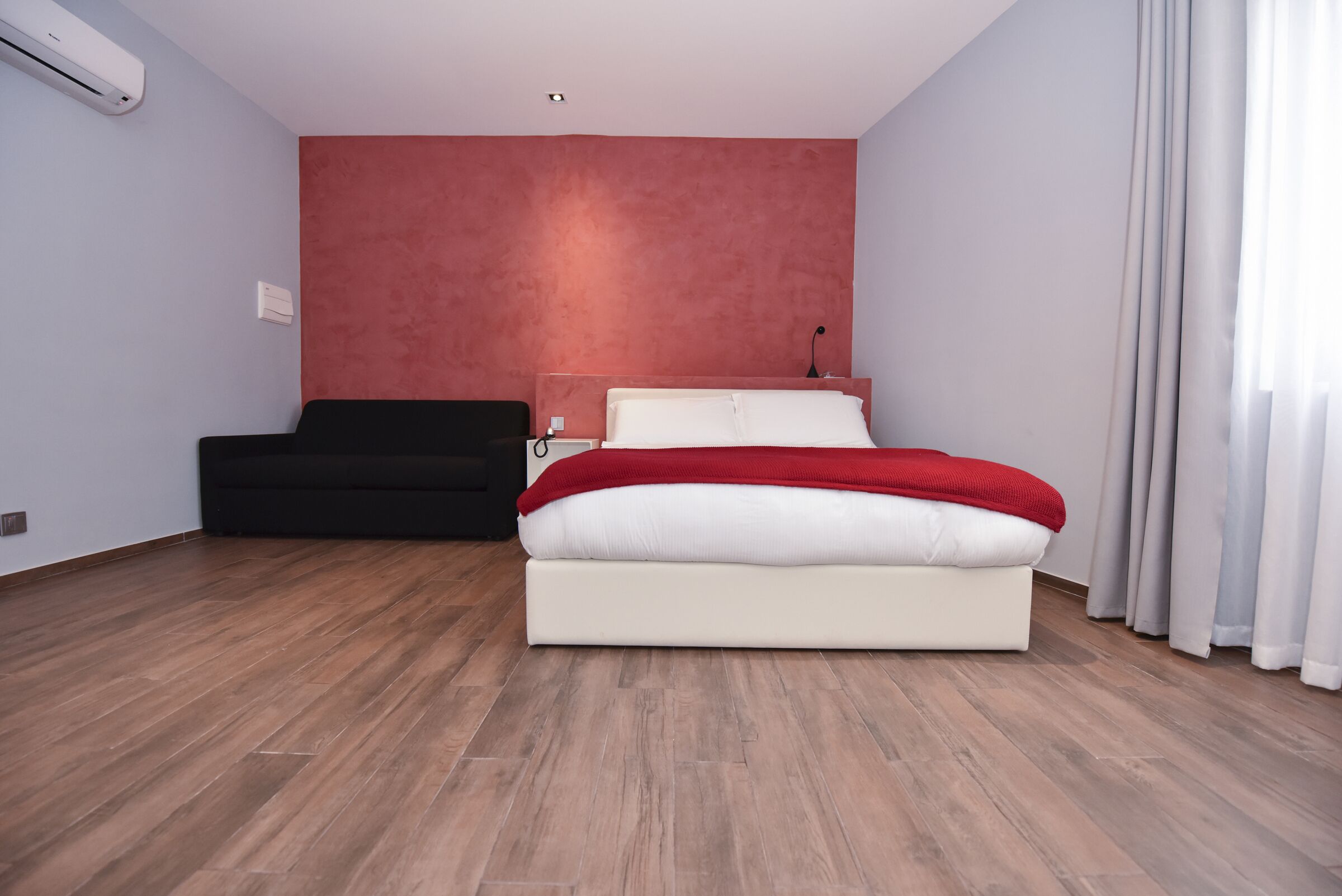 Un dormitorio moderno con cama, sofá negro y pared de acento roja.