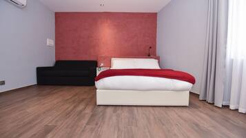 Un dormitorio moderno con cama, sofá negro y pared de acento roja.