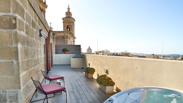 Terraza en la azotea con jacuzzi, dos sillas y una planta en maceta.