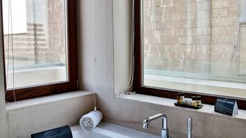 A modern bathroom with a large bathtub, two windows with blinds, and a towel rack.