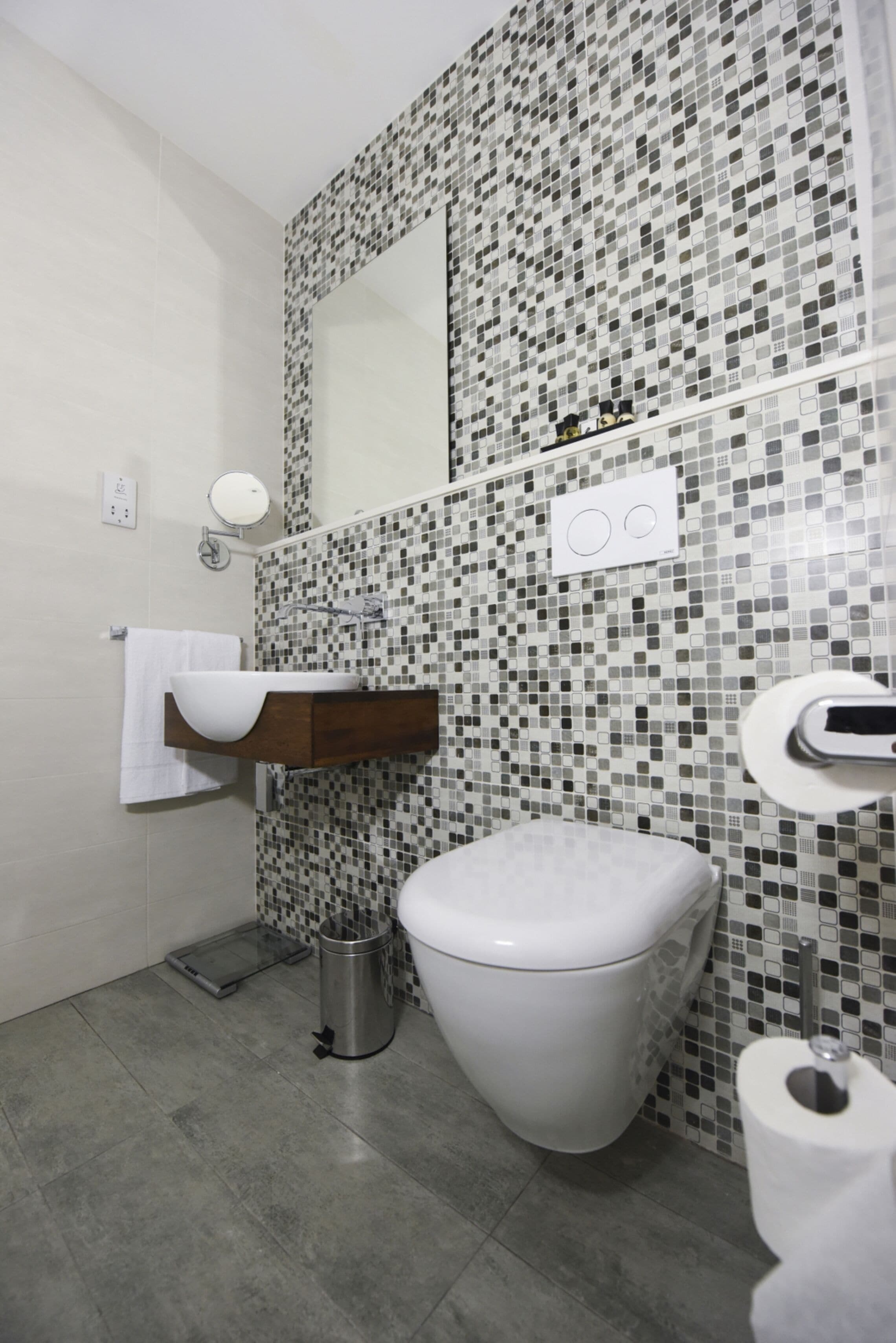Une salle de bain avec des toilettes blanches, un lavabo surmonté d’un miroir et un mur recouvert de carreaux.