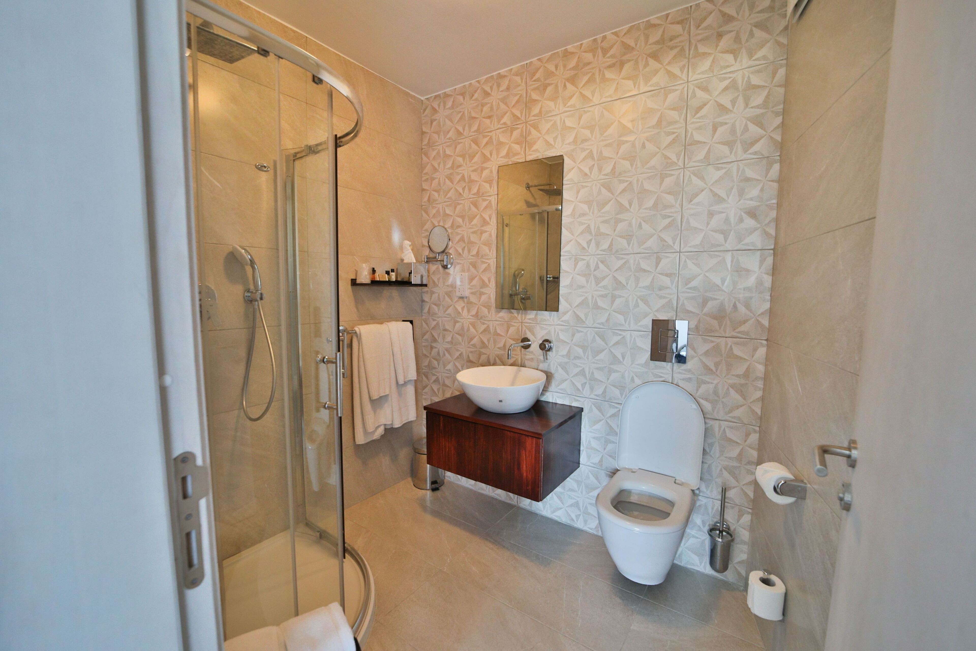 A modern bathroom with a glass shower enclosure, a white sink, a wooden vanity, and a toilet.