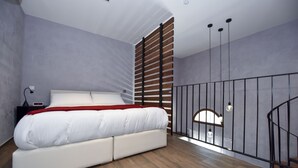 Un dormitorio con cama, piso de madera y una escalera con barandilla.
