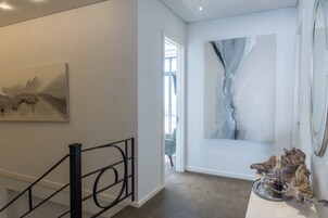A hallway with a staircase, a painting, a large abstract artwork, and a decorative piece on a table.