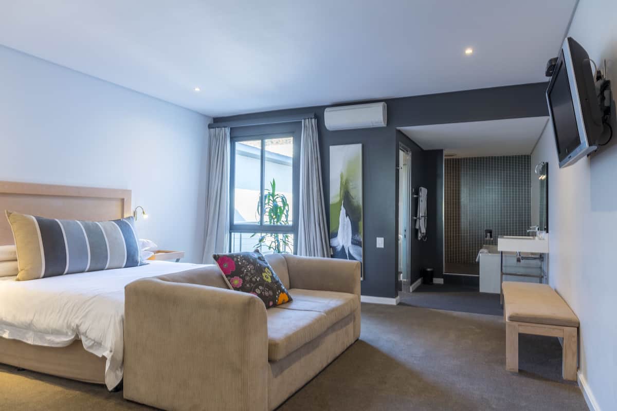 Una habitación de hotel moderna con cama, sofá, una mesita y un baño visible a través de una puerta abierta.