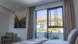 Une chambre d’hôtel avec un grand lit, une chaise, un tableau et une vue sur une colline et des bâtiments.
