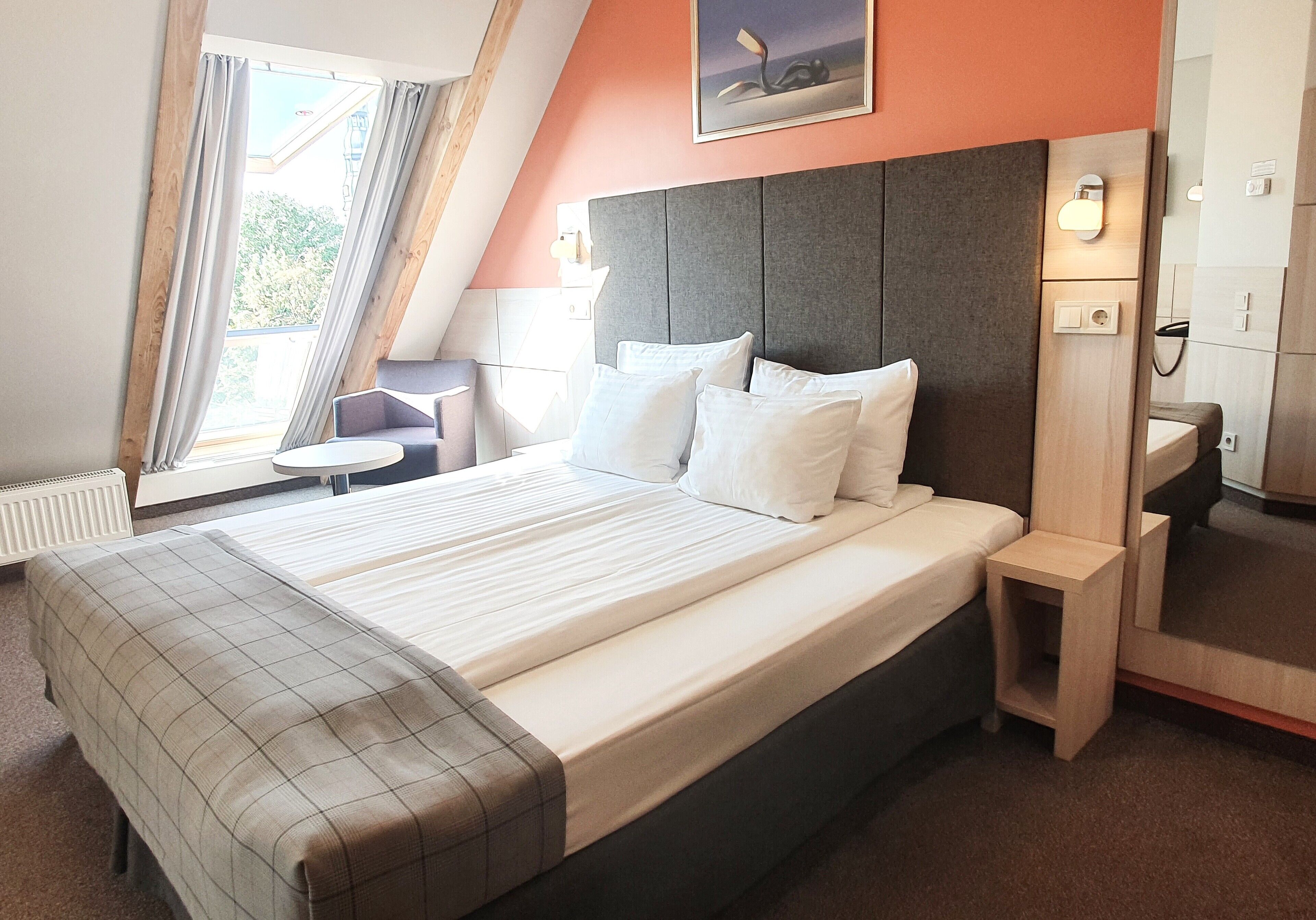 Ein modernes Hotelzimmer mit einem großen Bett, einem kleinen Nachttisch, einem Beistelltisch und einem Badezimmer mit Spiegel und Waschbecken.