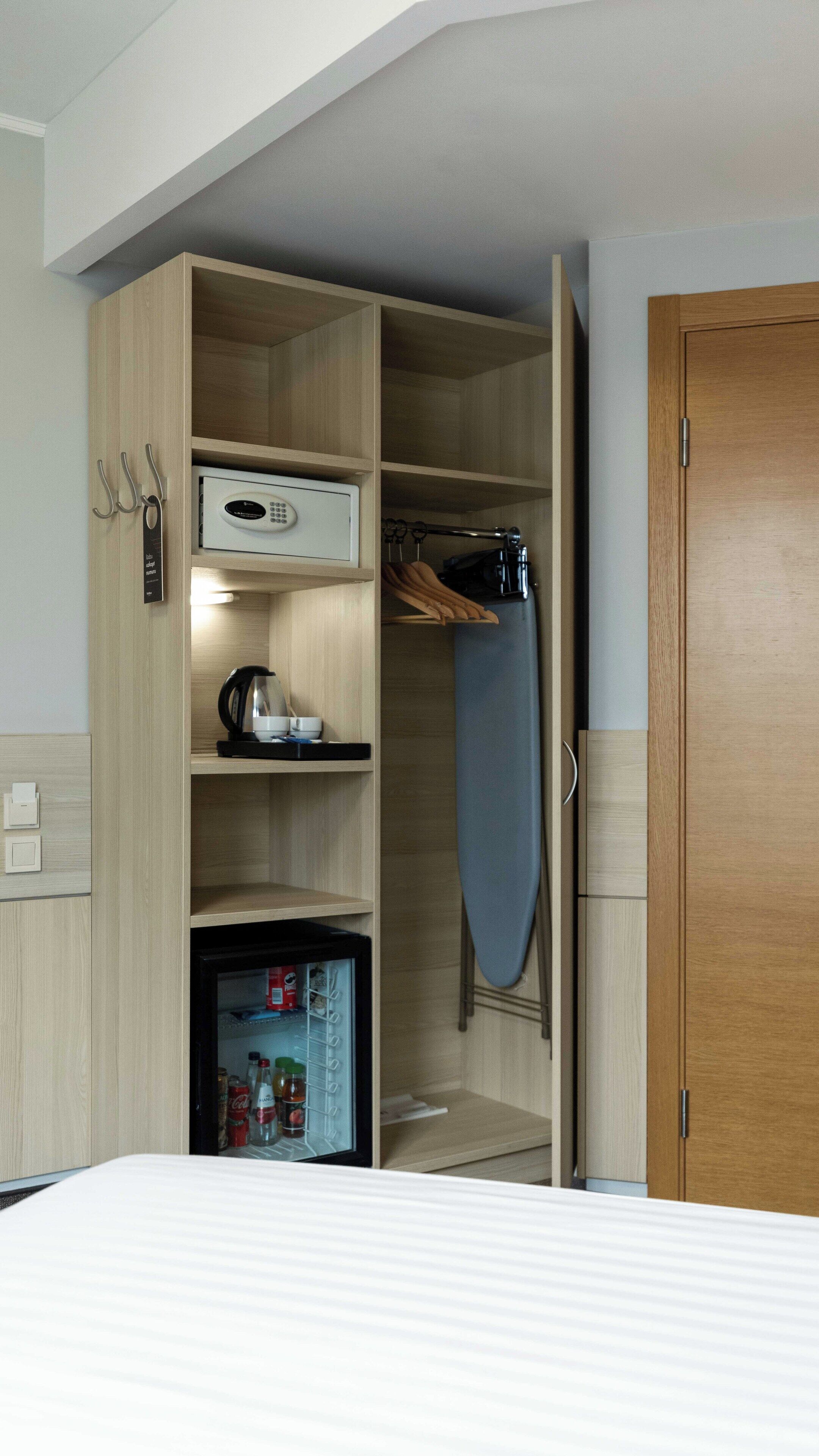 A hotel room with a wooden wardrobe, a small refrigerator, a kettle, and a microwave.