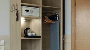 A hotel room with a wooden wardrobe, a small refrigerator, a kettle, and a microwave.