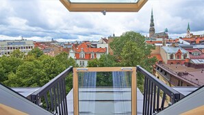 A balcony with a wooden railing and a glass door, overlooking a cityscape with historic buildings and a church spire. - Wellton Riga Hotel & SPA (Riga)
