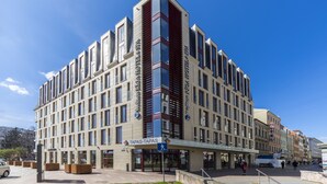 A modern hotel with a prominent entrance, multiple floors, and a clear sky.