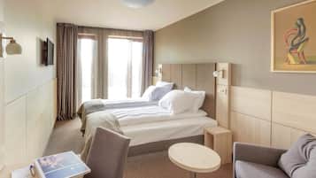Habitación de hotel con cama, dos mesitas de noche, escritorio con silla, una mesa redonda pequeña y un cuadro en la pared.