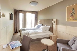 Habitación de hotel con cama, dos mesitas de noche, escritorio con silla, una mesa redonda pequeña y un cuadro en la pared.